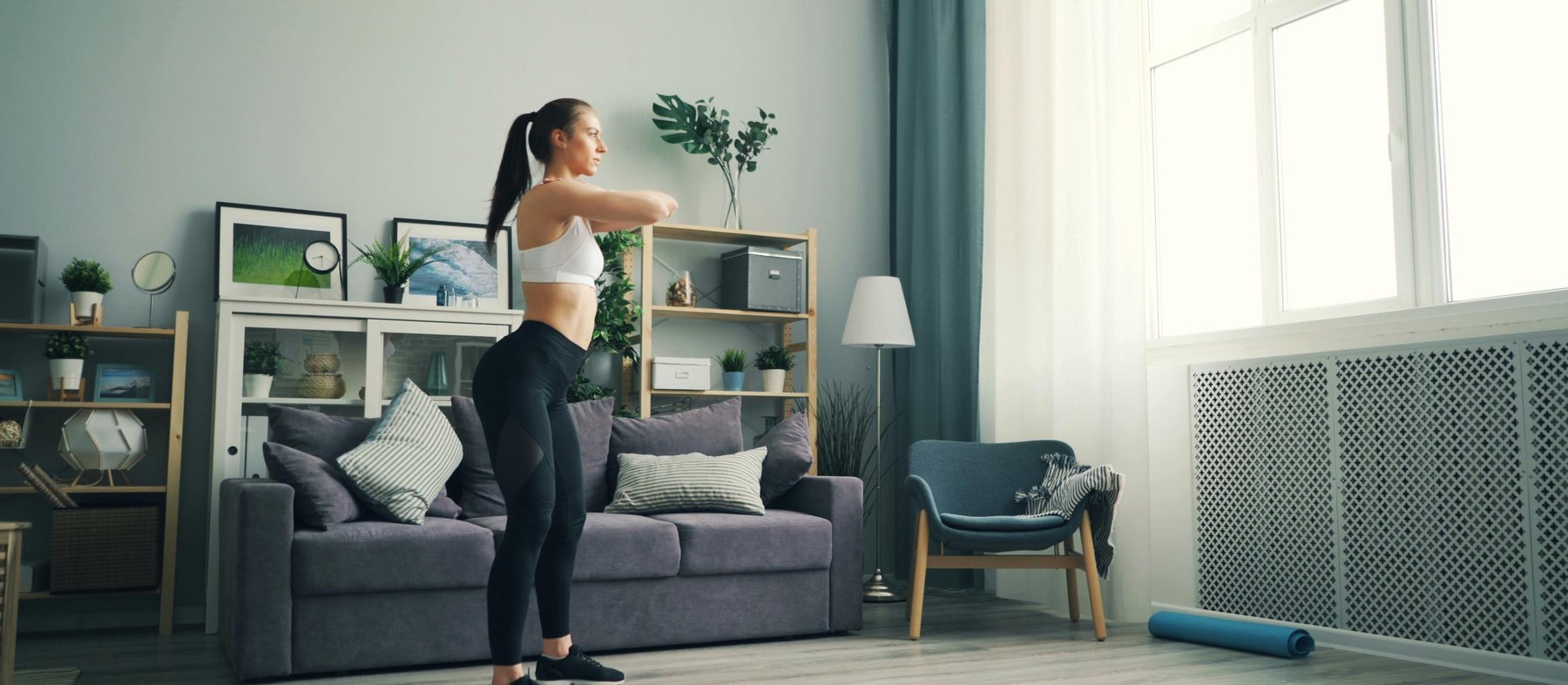 A woman mid-squat in a bright, lived-in living room with morning light through the window