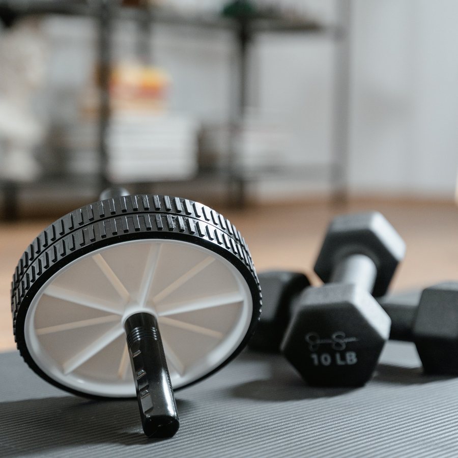 An ab wheel and a pair of black hex dumbbells resting on a grey mat