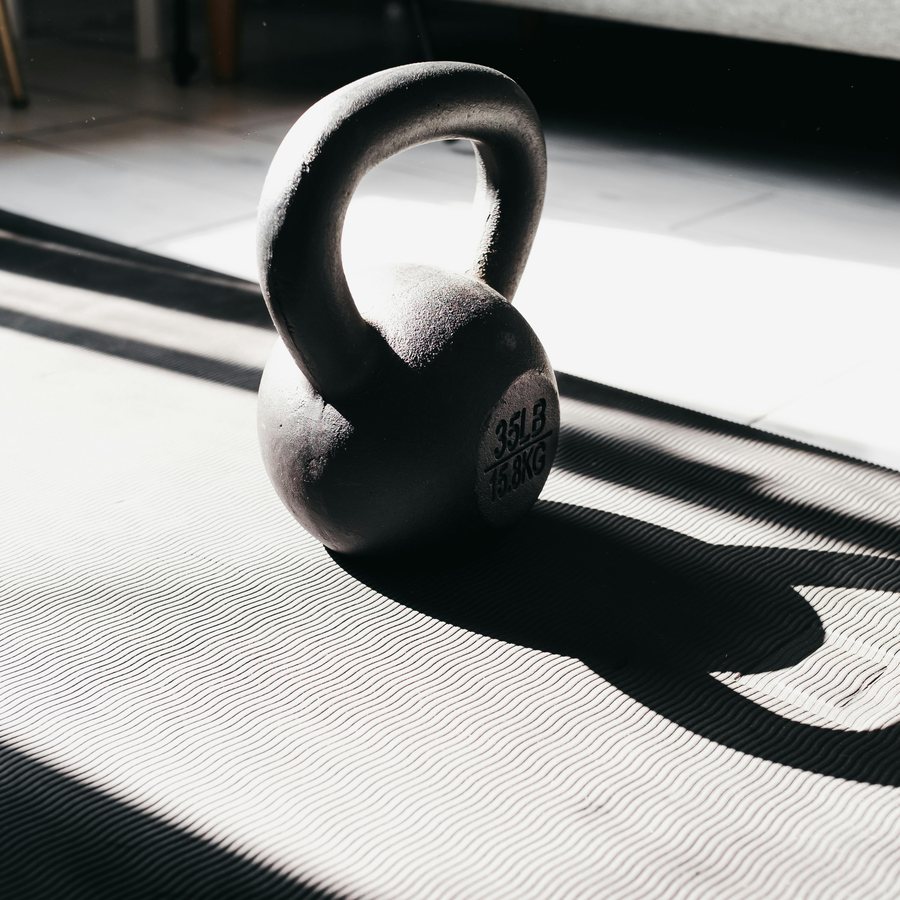 A cast iron kettlebell on a textured mat with strong window-light shadows